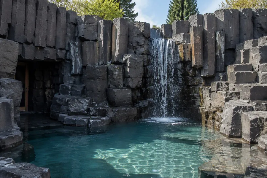 Künstlicher Wasserfall über Basaltfelsen in einen türkisfarbenen Pool